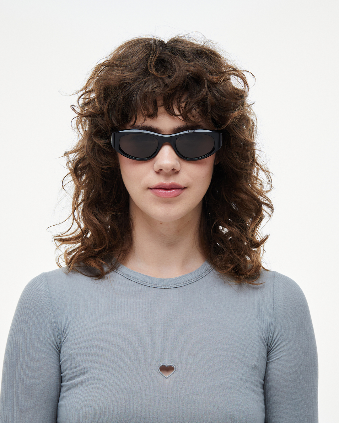 Woman wearing Pomé black oval wrap sunglasses with black lenses, look 3