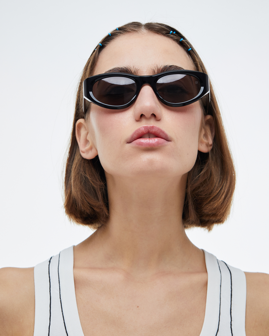 Woman wearing Pomé black oval wrap sunglasses with black lenses