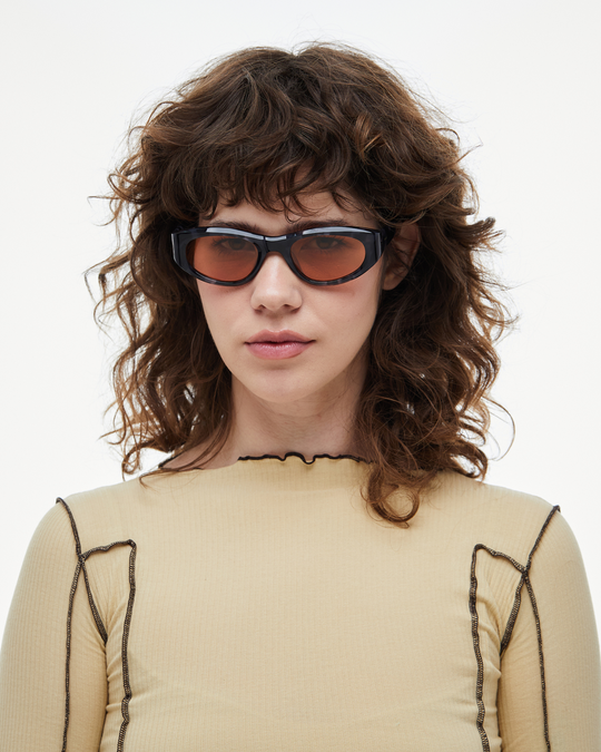 Woman wearing Pomé blue tortoise oval wrap sunglasses with orange lenses