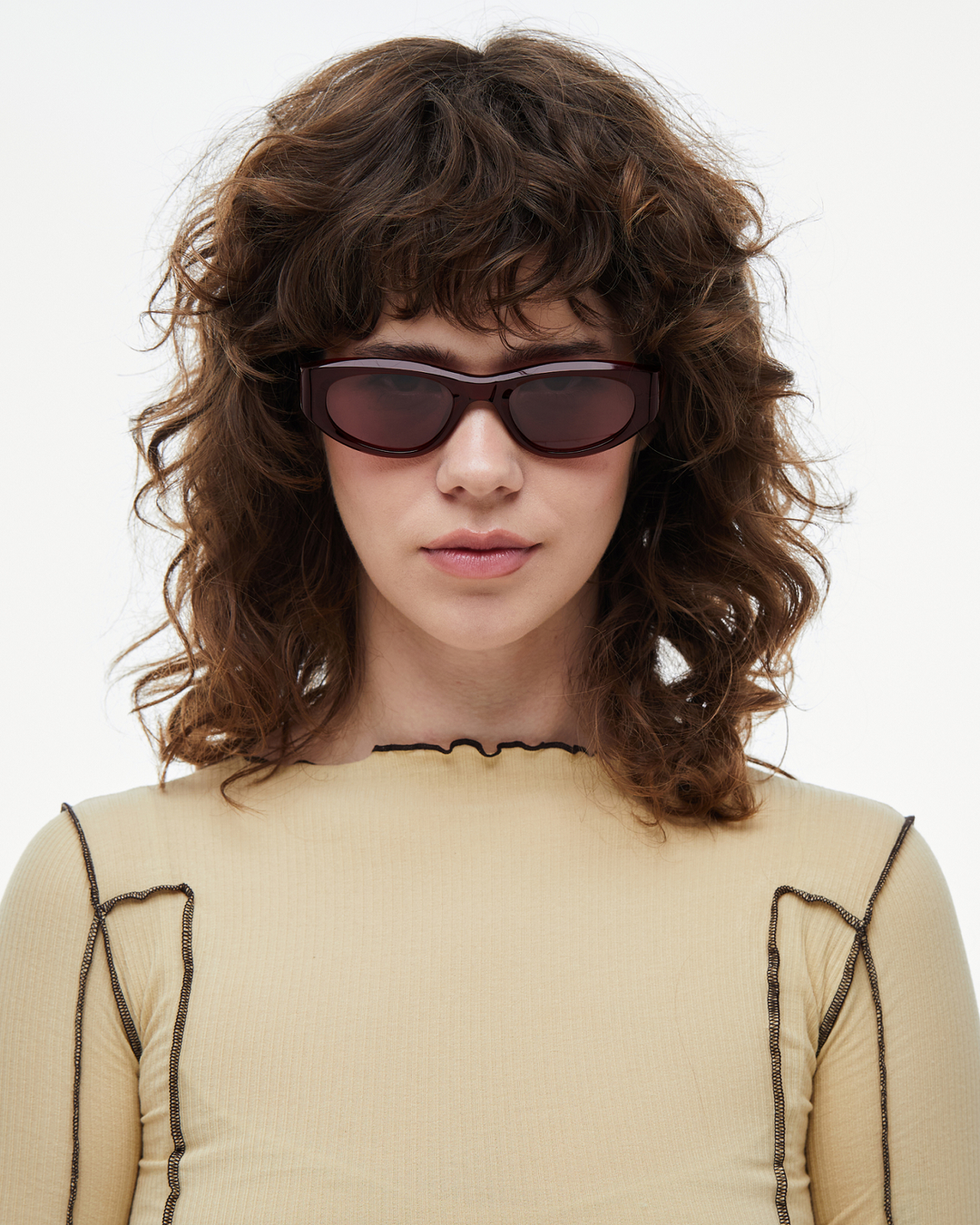 Woman wearing Pomé burgundy oval wrap sunglasses with red lenses, look 2