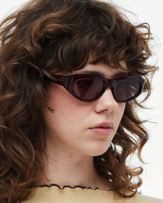 Woman wearing Pomé burgundy oval wrap sunglasses with red lenses